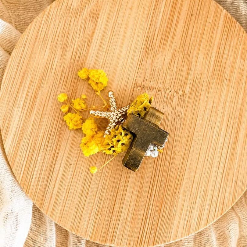 broche croix en métal doré avec perles blanches et fleurs jaunes séchées sur plateau en bois rond